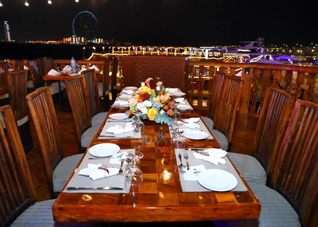 Guests dining on the upper deck of the Dhow Cruise Dubai Marina at night with the Marina skyline behind