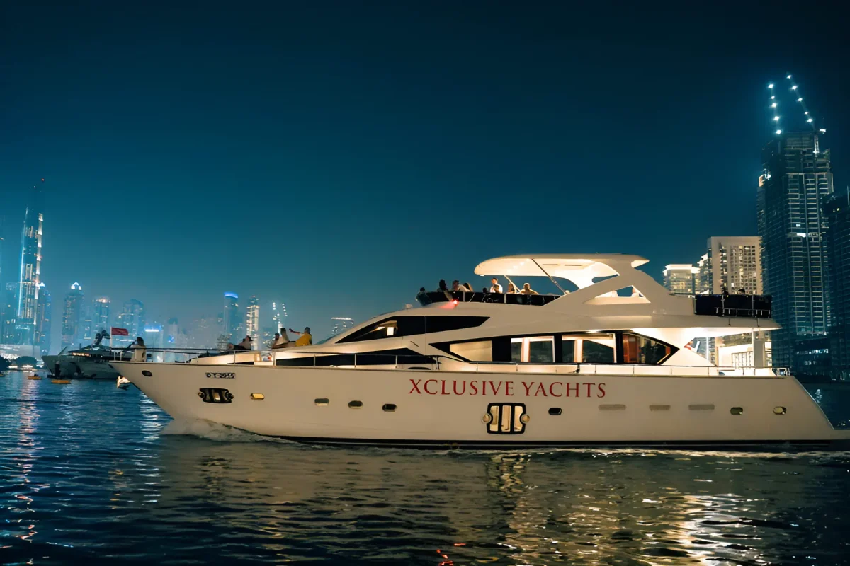 Xclusive Yachts motor yacht cruising Dubai Harbour at night with the Downtown Dubai skyline behind