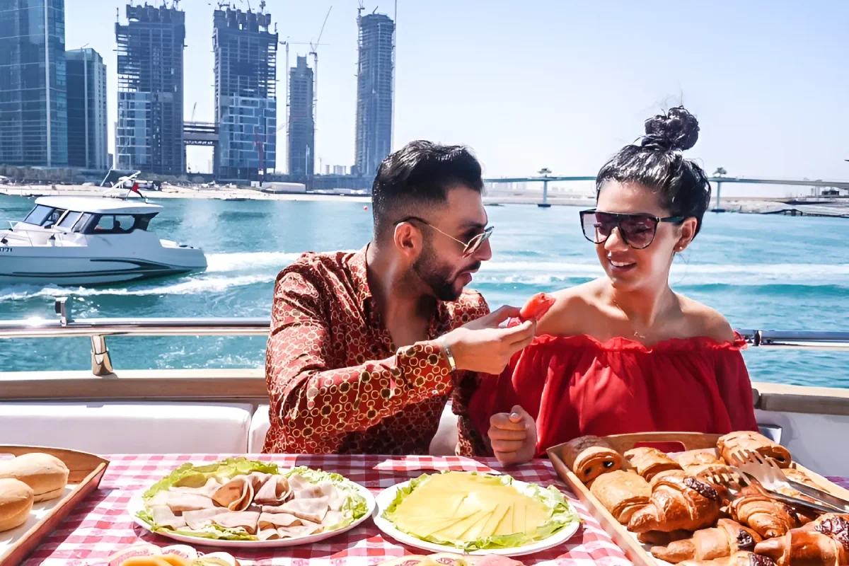 Couple sharing a breakfast spread of croissants and cheese on a yacht deck with the Marina skyline behind