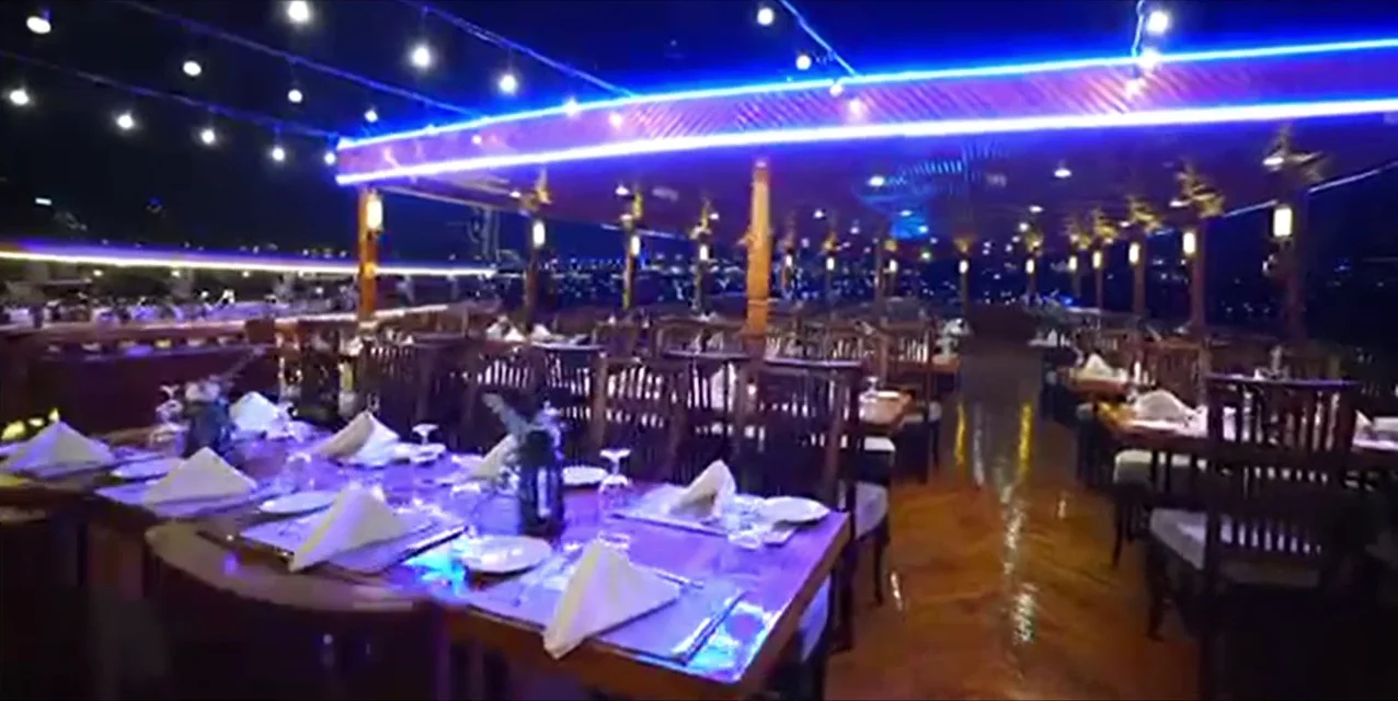 Guests dining on the upper deck of a dhow cruise at Dubai Marina at night, string lights overhead